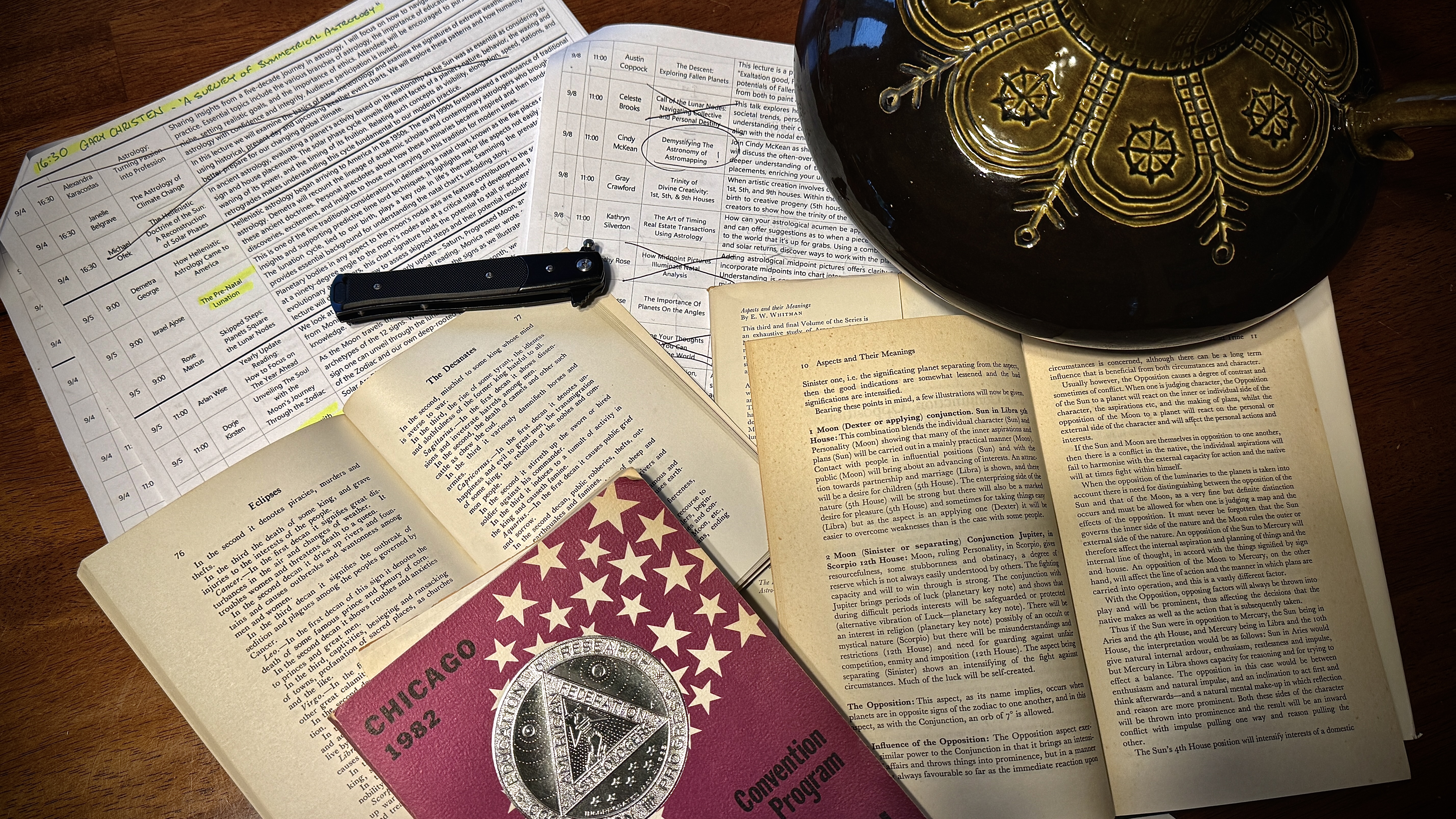Printed UAC seminar schedules with highlighter marks, astrology reference books, and a ceramic mug