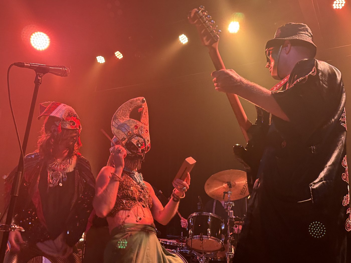 Both singers and bassist seen from below at the front row, warm amber stage lights overhead