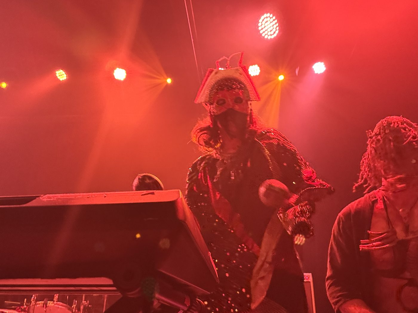 Masked singer and performer dancing on stage, red light, Bridgeworks