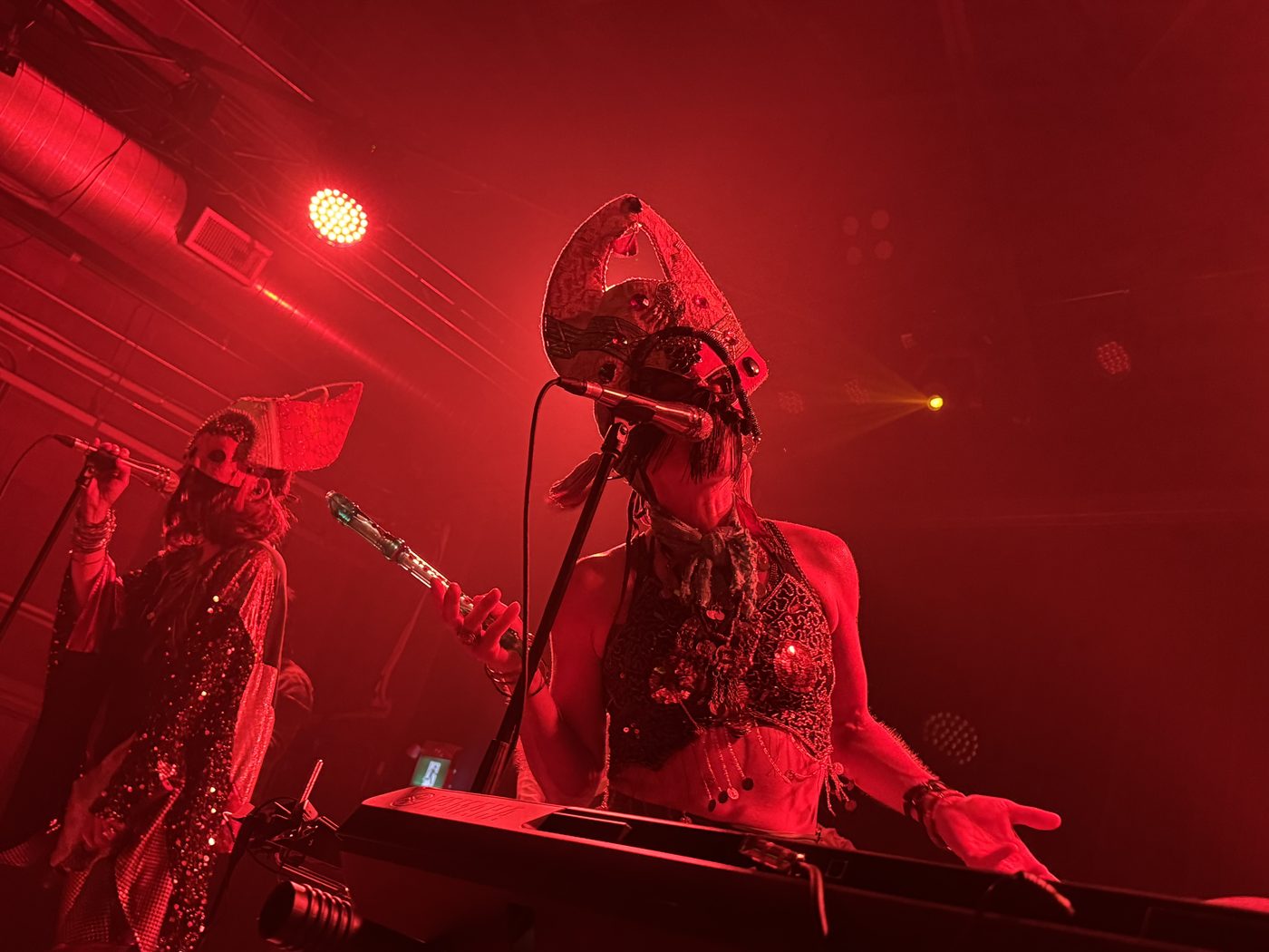 Two masked singers and bassist performing at Bridgeworks under warm amber light